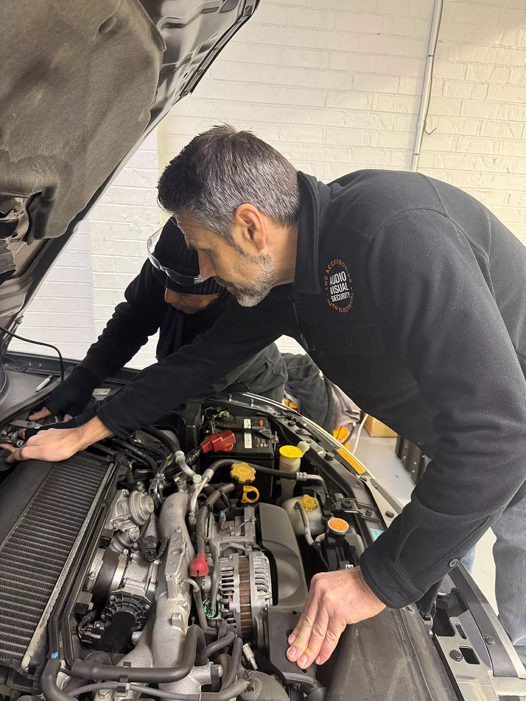 Mechanic working under a vehicle at Audio Visual Security workshop